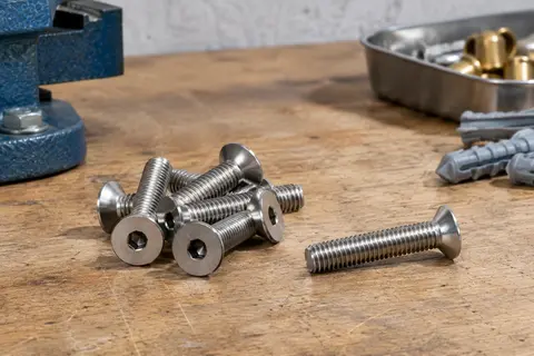 Vis métriques argentées en inox à tête fraisée et empreinte six pans creux, posées sur un établi en bois