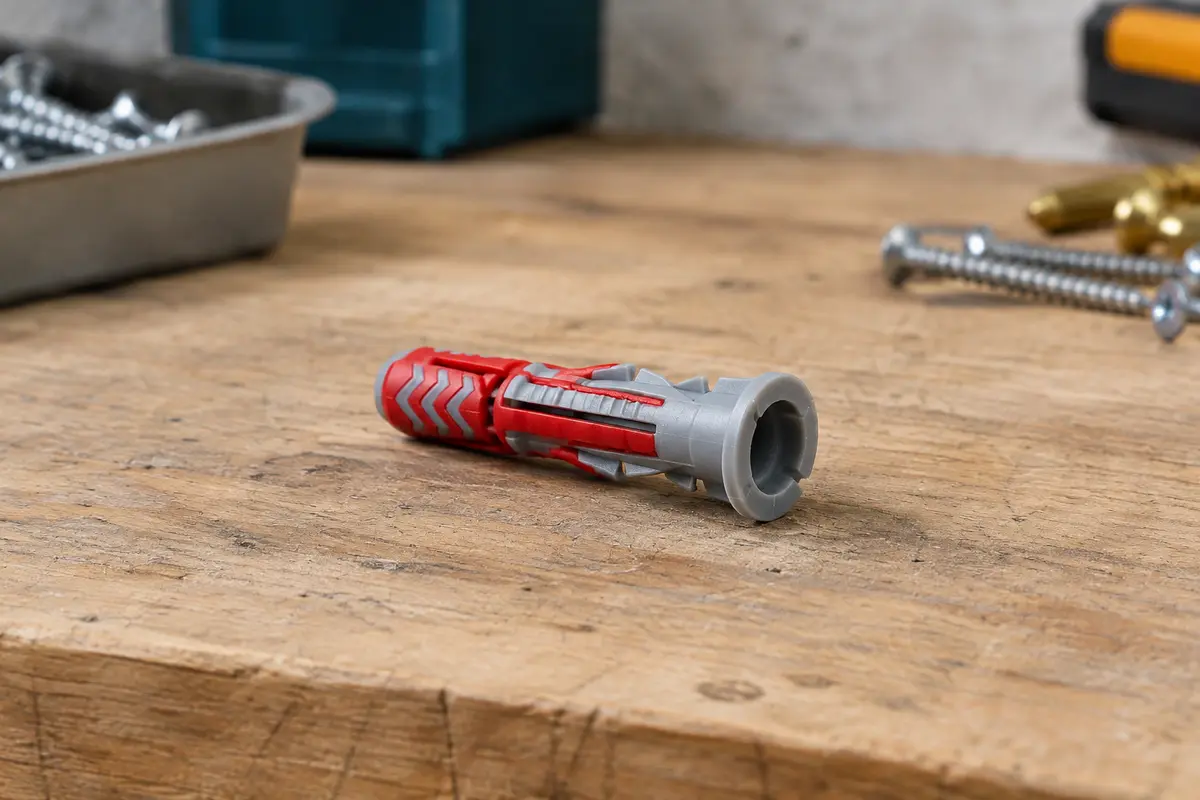 Cheville Fischer DuoPower bi-matière rouge et grise posée sur un établi en bois brut