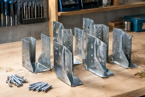 Lot de sabots de charpente galvanisés à ailes extérieures et perçages multiples posé sur un établi en bois