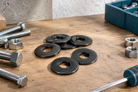 Rondelles plates noires en acier inoxydable disposées sur un établi en bois avec des vis et écrous