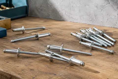 Rivets aveugles argentés en aluminium à grande tête disposés sur un établi en bois brut