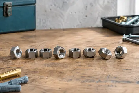Dix écrous hexagonaux en acier inoxydable A2 posés sur un établi en bois, filetages visibles.