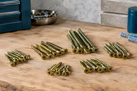 Assortiment de vis à bois en zinc jaune, à tête fraisée cruciforme, posé sur un établi en bois