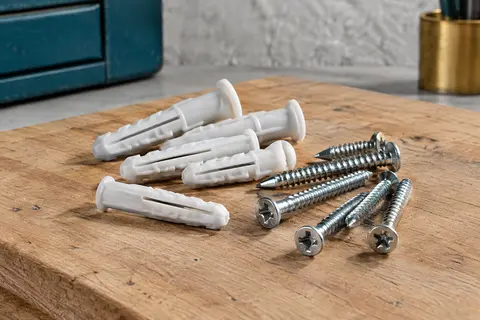 Chevilles à expansion en plastique blanc et vis métalliques disposées sur un établi en bois brut.